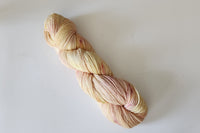A Skein of Hand Dyed Baby Alpaca Sport Weight Yarn in a pale yellow and pink variegated colorway twisted into a Skein 