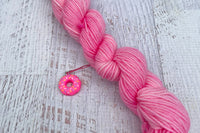 A mini Skein of Hand Dyed Merino Sock Weight Yarn and a coordinating stitch marker. Suitable for knitting and crocheting 