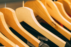 Eight wooden coat hangers are pictured. They are holding dark clothing. Picture is zoomed into the wooden coat hangers.