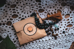 brown paper bag with round sticker next to a string of beads with a brown tassel all on a white crocheted doily
