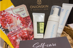 Contents of box showing sheet masks, suncare, cleanser, and moisturizer with Self-Care card in front.