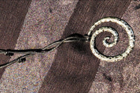 A textured metal swirl necklace on a black, adjustable cord with two knots displayed on a black background.