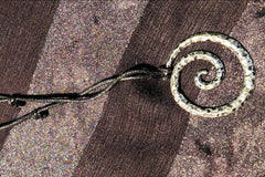 A textured metal swirl necklace on a black, adjustable cord with two knots displayed on a black background.