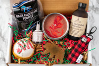 An open subscription box containing nail polish remover, candle, dark chocolate turtles, and nail polish.