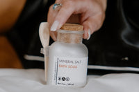 An apothecary jar of mineral salt bath soak that helps with detoxing and relaxation. Attached to the jar is a wooden scoop. 