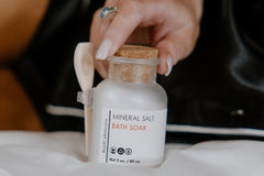 An apothecary jar of mineral salt bath soak that helps with detoxing and relaxation. Attached to the jar is a wooden scoop. 