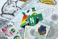Pic shows contents of a pack including coloring sheets, a sticker puzzle, stickers, postcards, and more. (Actual March 2021 pack.)