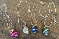 Wrapped Stone semi precious stones on a silver chain. Showing a pink, a clear, a dark blue, and a teal. 