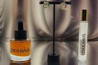LOKA.HAUS beauty: 'Duality Oil' in amber, center 'Intensity Parfum Roller', & luxe gold earrings on right. Elegance in a subscription box