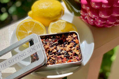 The Sipping Societea Loose leaf subscription tea tin with fruity caffeine free tea next to fresh lemons.