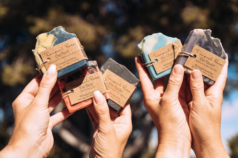 Hands holding a collection of Tranquil Rose handcrafted men's soaps featuring masculine scents, artisan designs and natural ingredients.