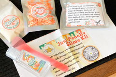 Components of the Peach Slime Kit including jello, glitter, and clay. Clear glue in a foil pouch with sticker labels.