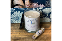 10oz candle and match tube sitting outside the gift box with other items included in the background. Product is sitting on a wooden tabletop