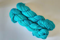 Two Skeins of Hand Dyed Baby Alpaca Sock Weight Yarn in a vibrant turquoise color against a light background 