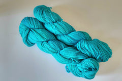 Two Skeins of Hand Dyed Baby Alpaca Sock Weight Yarn in a vibrant turquoise color against a light background 