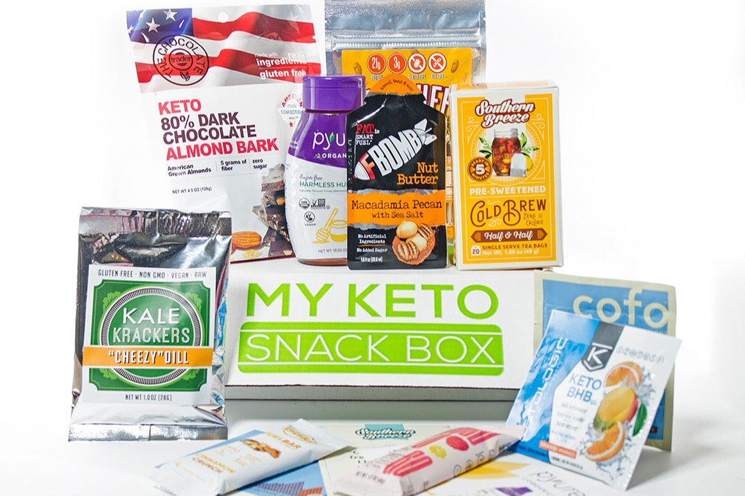 A My Keto Snack subscription box surrounded by kale crackers, dark chocolate almond bark, tea and nut butter. 