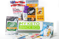 A My Keto Snack subscription box surrounded by kale crackers, dark chocolate almond bark, tea and nut butter. 