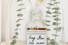 The Day Glow Serum by Greenmade goods. A bottle with golden serum dripping down over the label. Vases with succulents in the background.