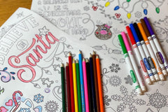 Coloring pages laying on the table along with markers and coloring pencils. Reindeer and Santa are the theme.