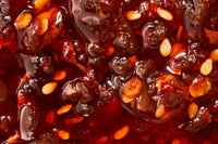 A blown up shot showing the crunchy and delicious flavors of chili crisp, floating around in oil. Garlic and chilis for days