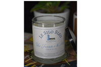 Day at the Sea candle with black lid resting on the side of the candle. They are on a stack of French magazines with potted plants behind