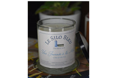 Day at the Sea candle with black lid resting on the side of the candle. They are on a stack of French magazines with potted plants behind