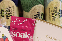 Yarn Shop Mystery Box featuring three skeins of Frog Tree Alpaca Sport yarn in green, navy, and teal with craft accessories