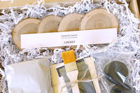 An open Crate Club box displaying 4 cherry wood coasters, sealants, an applicator brush, and other box ingredients.