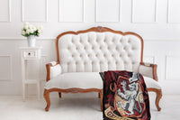 An all white room with a white side table, white flowers and an elegant white couch with a Gryffindor Tapestry Throw blanket on it.