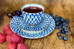 An antique tea cup full of deep red fruit tea surrounded by fresh berries for The Sipping Societea Loose leaf tea subscription box