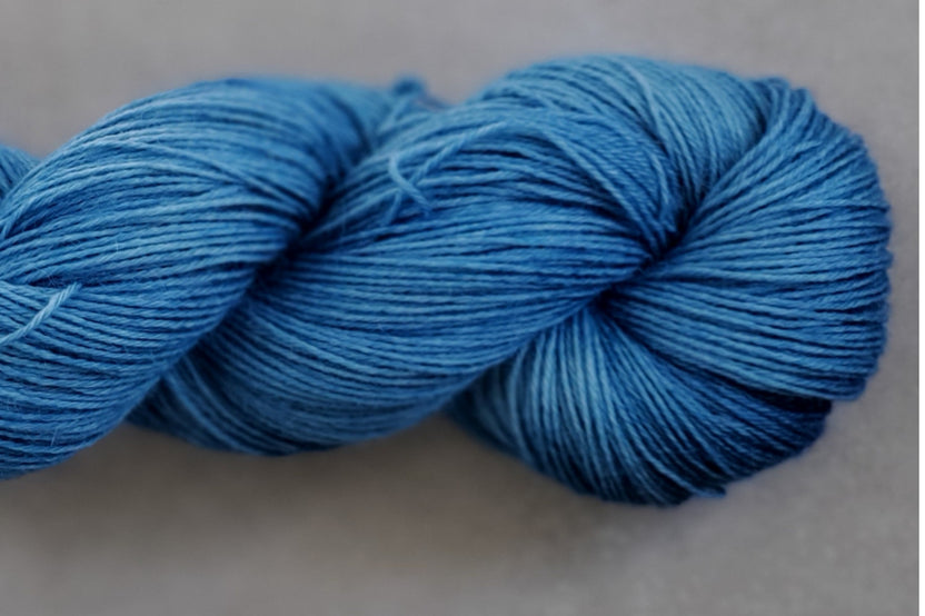 Close up photo of a hand dyed skein of sock weight yarn against a solid background. The skein is twisted and shows a variety of color.