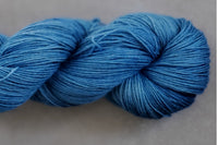 Close up photo of a hand dyed skein of sock weight yarn against a solid background. The skein is twisted and shows a variety of color.