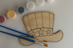 Patriotic hat with stars and stripes wooden shape. There are also two paint brushes and a paint sampler.
