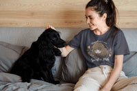 Lady sitting on a bed and petting her black dog. She is wearing a grey blue Hermione Granger Tshirt.