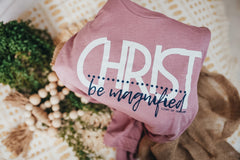 The tee features a prominent design in white and navy, proudly displaying the powerful message, "Christ be Magnified."
