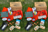 Wild Woman Box subscription boxes stacked on a mountain ledge with a scenic view in the background
