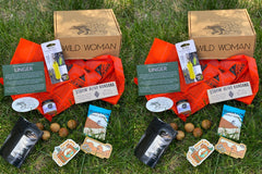 Wild Woman Box subscription boxes stacked on a mountain ledge with a scenic view in the background