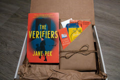 Book titled the Verifiers by Jane Pek resting in box next to book wrapped in brown paper and twine stuffed with items