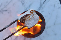 A perfectly chard marshmallow on a roasting stick being roasted over the city bon fire portable bon fire. 
