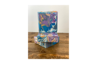 Stack of Coastal soap on a wooden table with white background. The soap is swirled in blue, purple and gold.