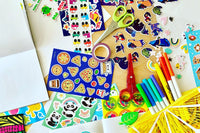 A craft table is pictured, with scissors, notebooks, markers and lots of stickers for a fun afternoon of kids crafting.  