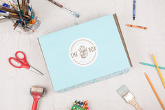 Outside the Box Creation's kids art box in its signature light blue color surrounded by art supplies on a flat surface