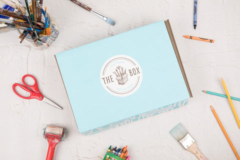 Outside the Box Creation's kids art box in its signature light blue color surrounded by art supplies on a flat surface