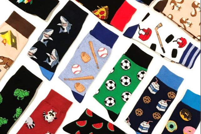 Many socks from the Say it with a Sock subscription box, laid out neatly. There are shark, baseball, soccer and frog socks.