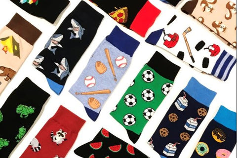Many socks from the Say it with a Sock subscription box, laid out neatly. There are shark, baseball, soccer and frog socks.