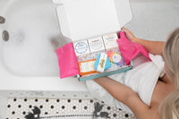 woman sitting on the edge of the bath tub with Bath Bevy Subscription box with bath bombs, whipped soap scrub, aloe gel and soap
