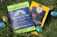 Bag of Kalahari Biltong, bag of Aufschnitt's Teriyaki jerky, lying on the grass outside, surrounded by several shiny Easter eggs. 