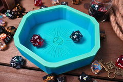 A green blue 3d printed dice tray that is a hexagon and has a d20 design and several TTRPG dice scattered around it and inside of it.