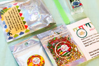 Ugly sweater slime kit contents in a flat lay, glitter, jello, instructions, glue and activator. Red and green theme