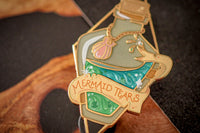 Gold plated, hard enamel pin depicting Mermaid tears, 2 colours mixed swirl enamel in a translucent enamel bottle. 